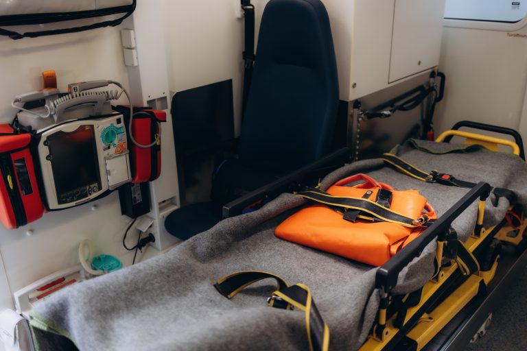 Wnętrze karetki pogotowia z kocem i pomarańczową torbą na noszach transportowych.